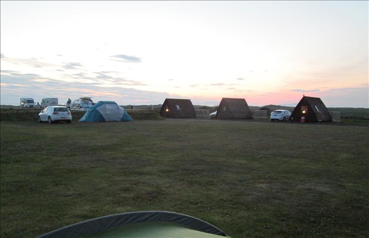 The light is fading over tents, pods, campervans and caravans at the site