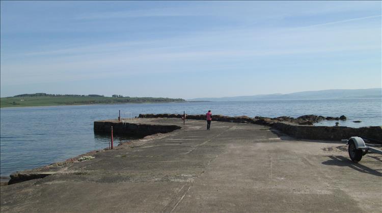 Sharon stands on a small harbour wall overlooking a very calm Clyde estuary