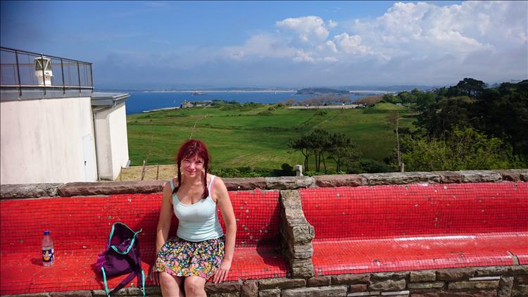 Sharon in vest top and skirt sitting beside the large white lighthouse at Cabo Mayor