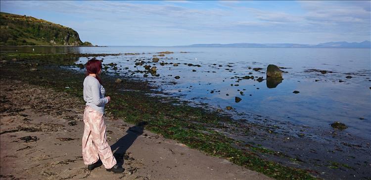 Sharon stands on a rugged stone and sand beach looking out to see on a totally calm morning