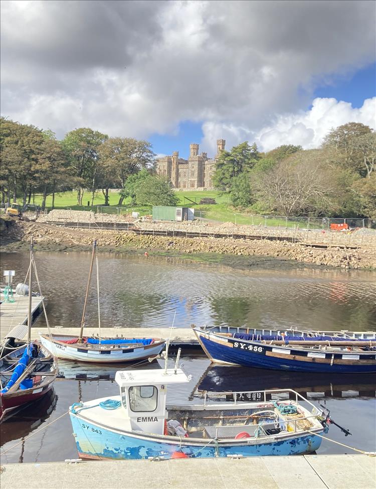 Across boats in the water and some construction we see a large castle style stone building