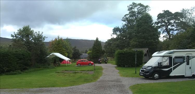 The skies are mixed with dark clouds and blue patches, we see the bikes and the campsite at Strontian