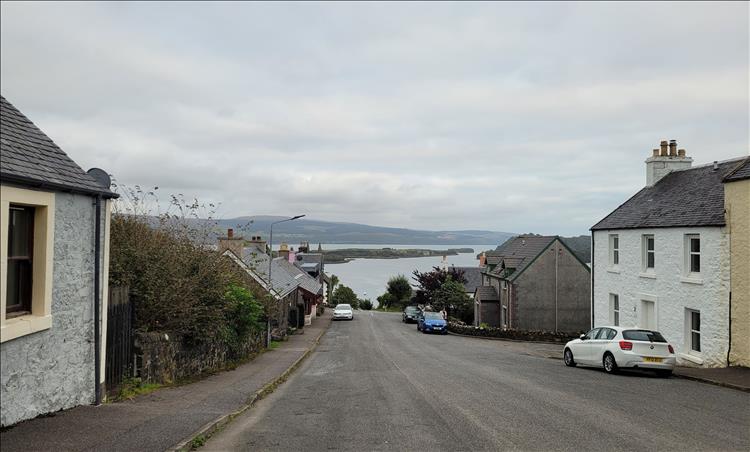 A lane with small older and faded houses and a view over the bay at Tobermory