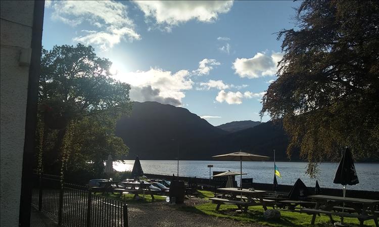 Across the outside table and chairs of the pub is the road and the loch and more mountainous Highland scenery