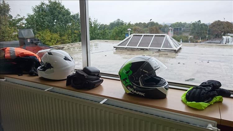 2 helmets on a window overlooking the wet roof of a dull motorway services