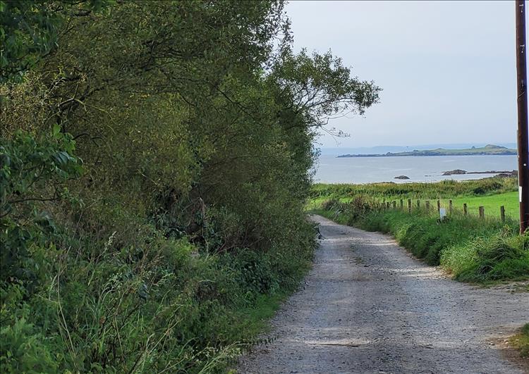 A plain gravel road leading away to the sea and shoreline in the distance