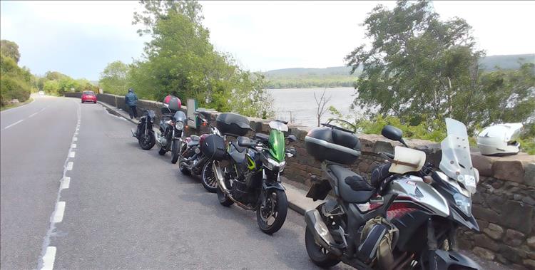 5 motorcycles in a parking area beside the scenery of Loch Ness in Scotland