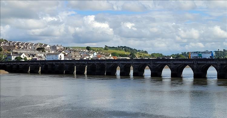 A low and old bridge with many arches crosses a calm river in Bideford