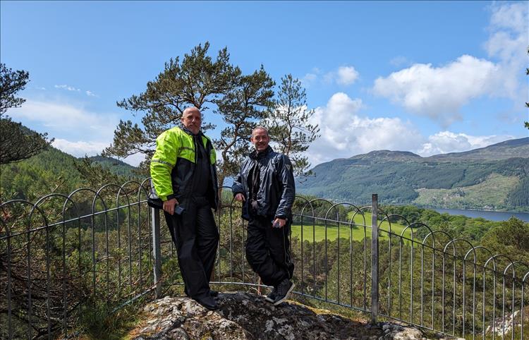 Rik and Rob by a railing with blue skies and the beautiful scenery of loch ness