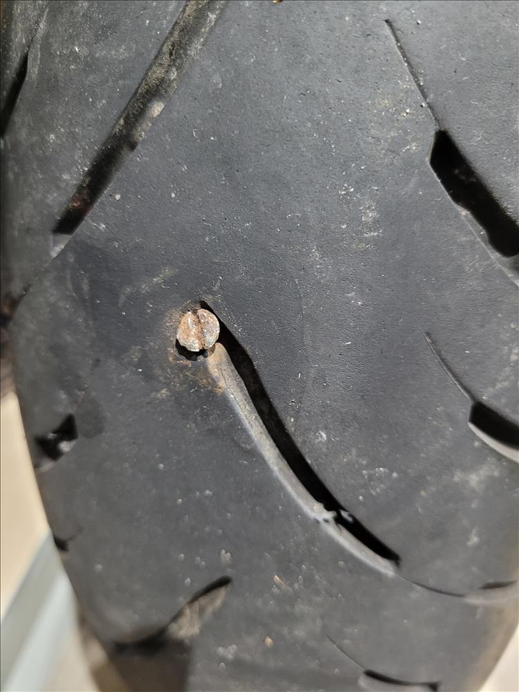 The rear motorcycle tyre with a screw right through the treads causing a puncture