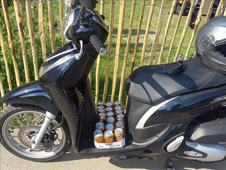 A pack of tinned beer on the footboard of a step through scooter