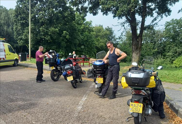 The middle aged and a bit tubby men pose or tinker with their small motorcycles in a car park