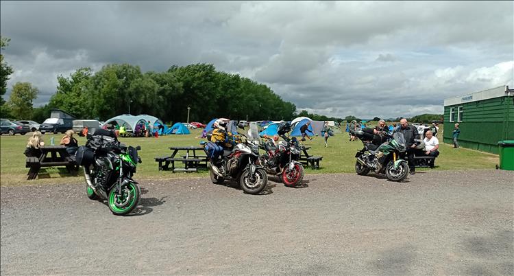 Motorcycles on a gravel car park, various tents and youths behind them at the race circuit