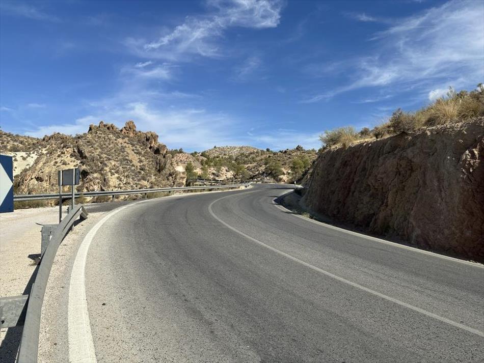A curve in the road, smooth tarmac, steel barriers and dry arid hardy land either side