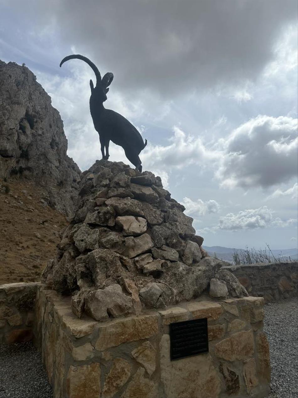 A stone statue of a goat with long horns atop a pile of stones