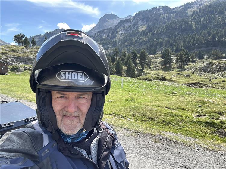 Andy with flip up helmet open looks at the camera with the stunning backdrop of the pyrenees