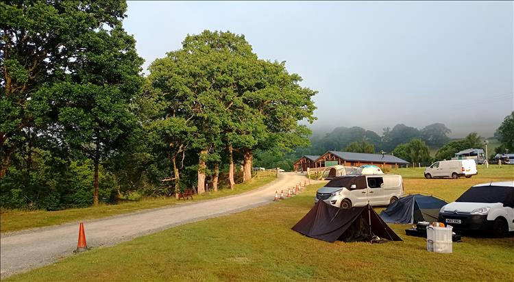 Tents and cars, trees and the river, and mist over the hills beyond