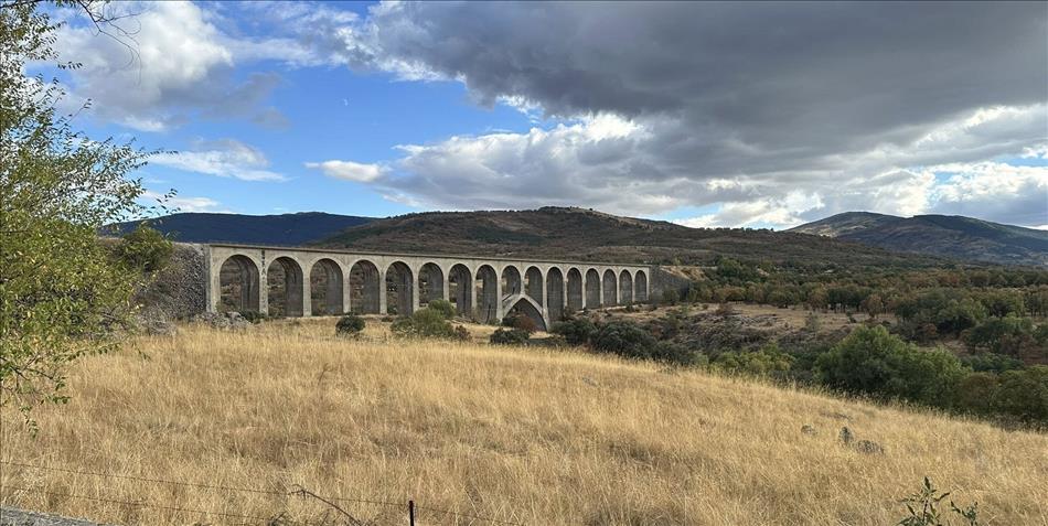 many arches form a railway bridge across the countryside between the mountains