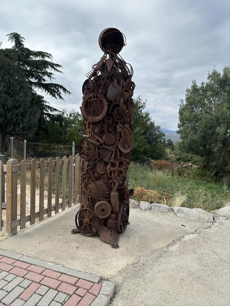 A tall slender sculpture seemingly made up of scrap steel items like shovels and wheels