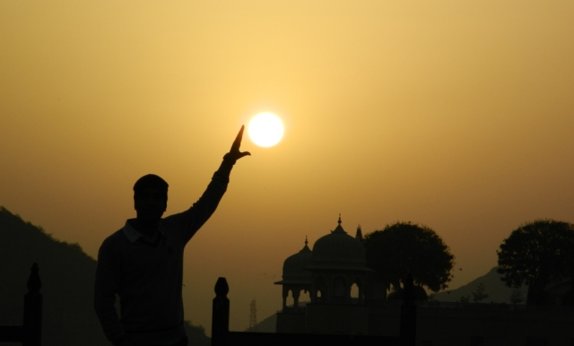 arjun in outline holding his hand up, with the sun between his fingers in india