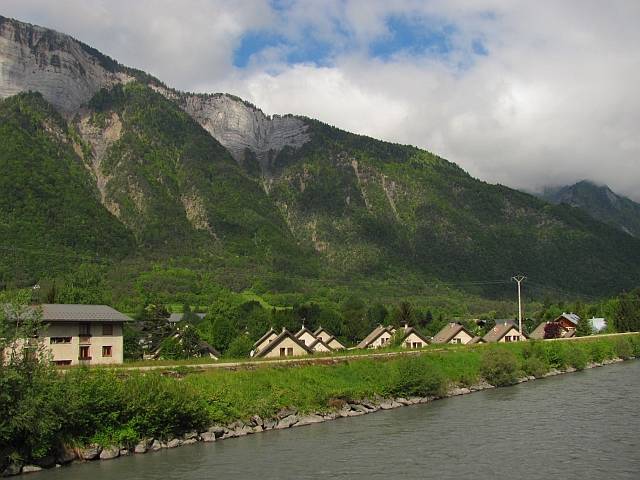 romanche river and valley floor, mountains to the side, lush green trees and alpine houses at le bourg d'oisans