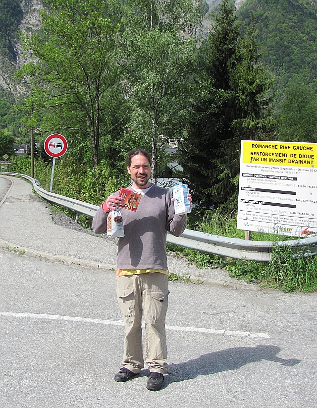 the bf holding boxes and bags with breakfast foods by the trees and roads into le bourg d'oisans