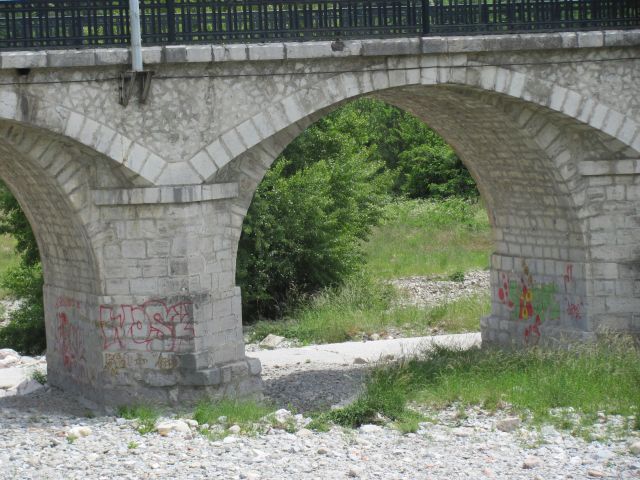 old stone built bridge over dry river bad with some graffiti under the arches