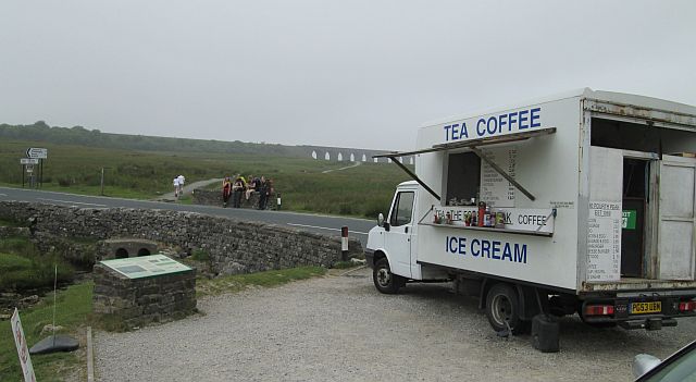 a butty van in the forground and the ribblehead viaduct in the mist in the distance, some walker in the mid ground