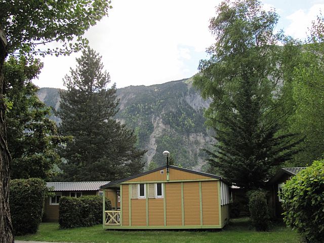 small wooden chalets between trees and mountains in the background at la piscine campsite