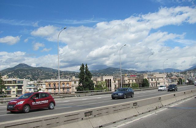 a sunny dual carriageway with a large town below which is Nice on the Cote D'Azur