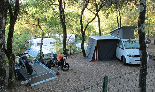 a vw campervan with awning and 2 motorcycles by a motorcycle trailer at the campsite