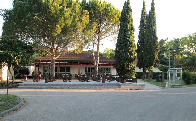 trees around a patio area and a bar in the sun, but with no people at la bastice campsite nimes