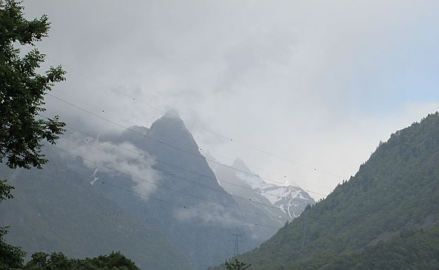 mountains covered in mist with trees in the foreground on the road to Le Bourg-d'Oisans, France