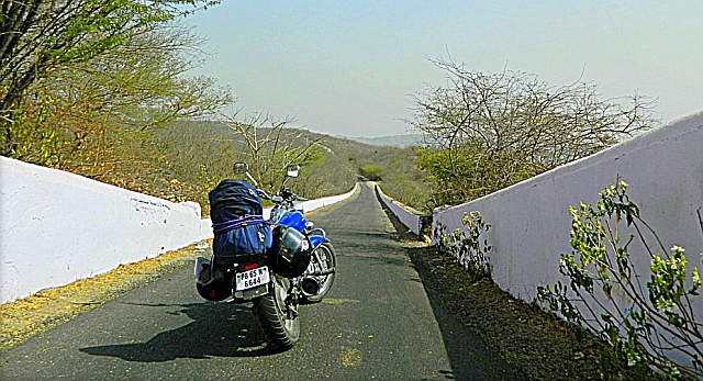 a loaded motorcycle on a long narrow coutryside lane in india