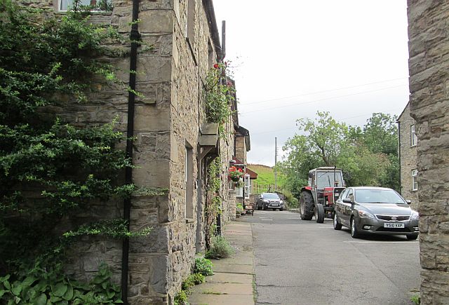 stone cottages with cars and a tractor parked in the lane in hawes