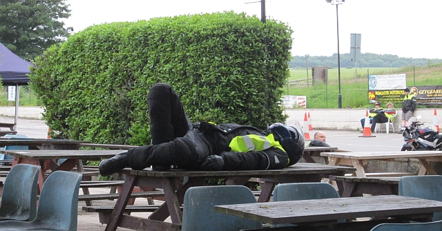 A very tired motorcyclist still wearing his bike gear and helmet sleeps on a table