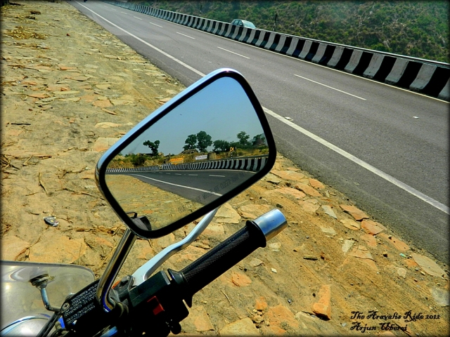 a warm dry indian road reflected in a motorcycle mirror