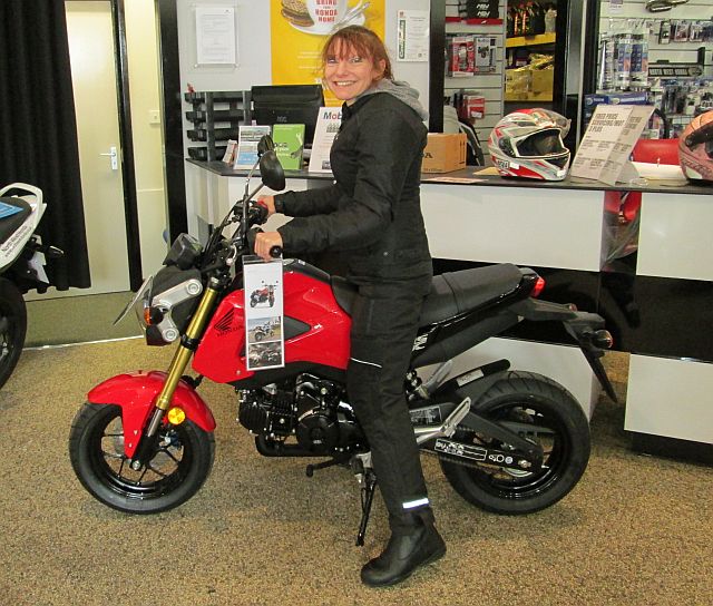 sharon sitting astride the honda msx 125 with her feet on the ground in a showroom