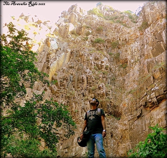 arjun standing before sand coloured sheer cliffs