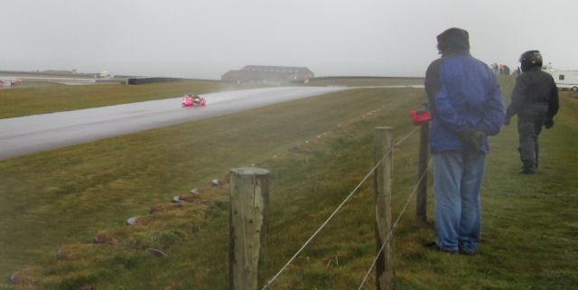 a rain soaked track at anglesey circuit with a sidecar as wet people watch