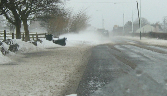 a main road with a swirl of snow being blown into a drift