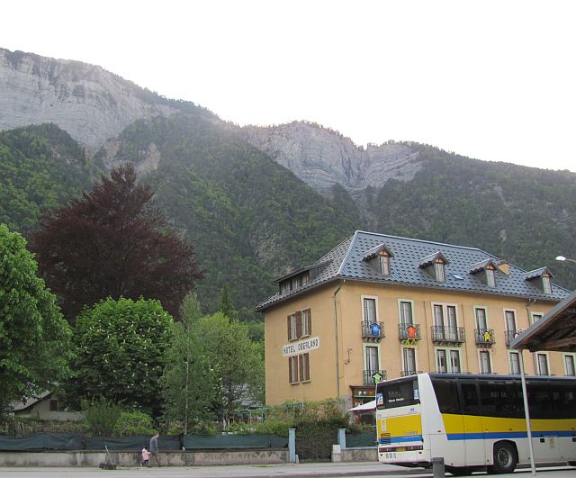 a bus in a terminus and a hotel, with vast soaring rocky mountains behind at le bourg d'oisans