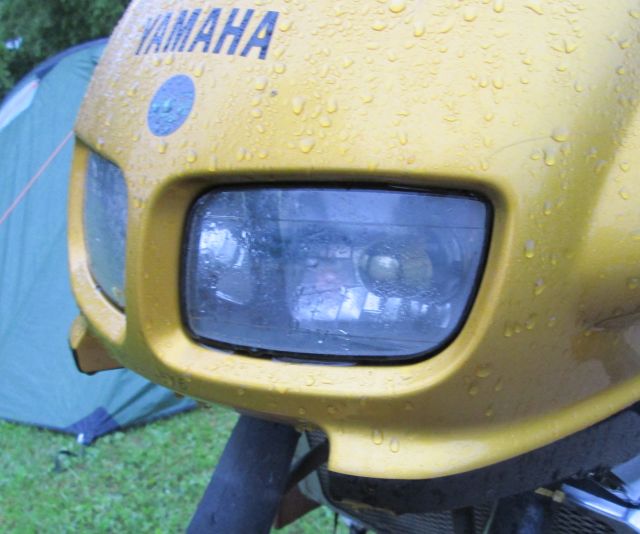 the headlamp reflector on a rain soaked bike with a wet tent behind in Auxonne france