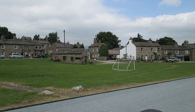 the large village green with shop in the distance and stone houses all around at west burton, yorkshire dales