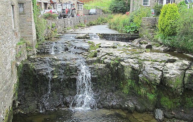 a small river cascading over rocks and a short waterfall in the centre of hawes in the dales