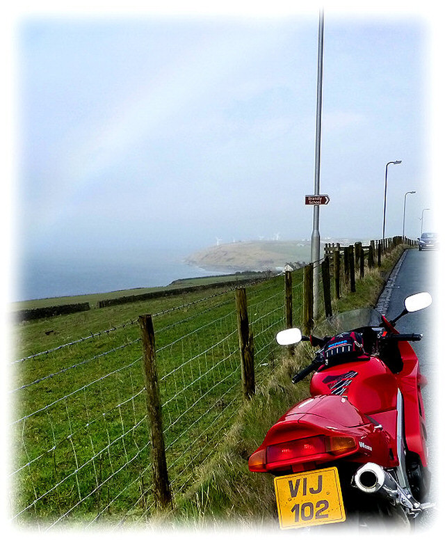 motorcycle beside a road looking over hills and almost a rainbow