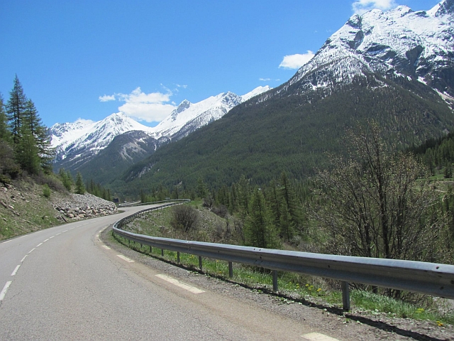 an alpine road snaking through snow capped mountains and tree lined hillsides