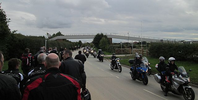 bikers walk to the left, motorcycles arrive to the right of the image