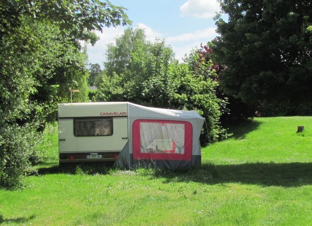 a caravan and awning with long grass all around in the trees at chinon