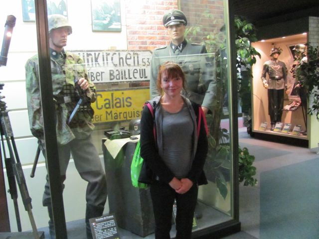 sharon stands in front of a glass cabinet filed with world war 2 uniforms on display